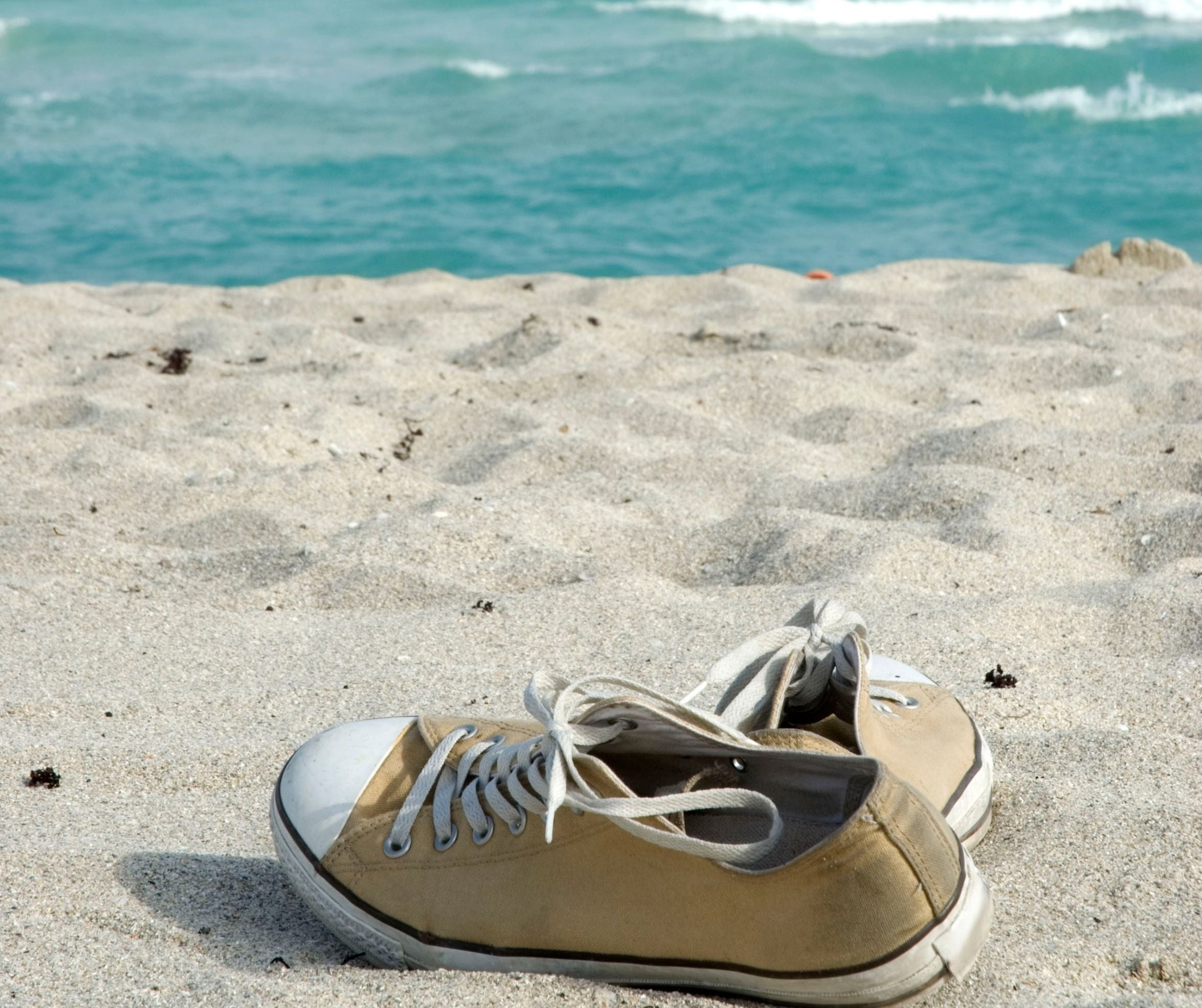 pair of old sneakers on the beach with the ocean in background